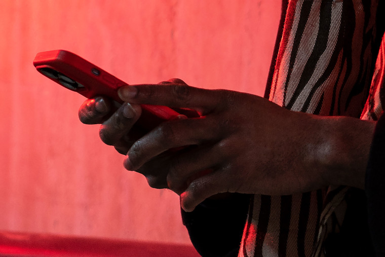 Image: A man holds a smartphone while standing near a wall with red neon lighting