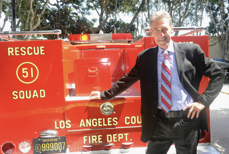 Randolph Mantooth rests one hand on a vintage red fire engine.