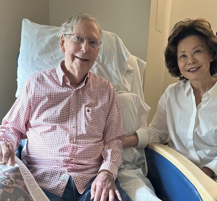 Mitch McConnell smiling with his wife while seated against a stack of white pillows.