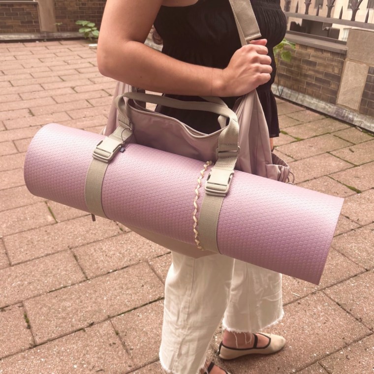 Woman holding Calpak gym duffel with a rolled up yoga mat attached to it.